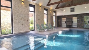 An indoor swimming pool with stone walls, wooden beams, and a seating area with chairs. - Domaine des Cyclamens (Verneuil-sur-Indre)