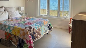 Ein Schlafzimmer mit einem großen Bett, einem Fenster mit Meerblick, einem Deckenventilator und einer Holzbalkendecke.