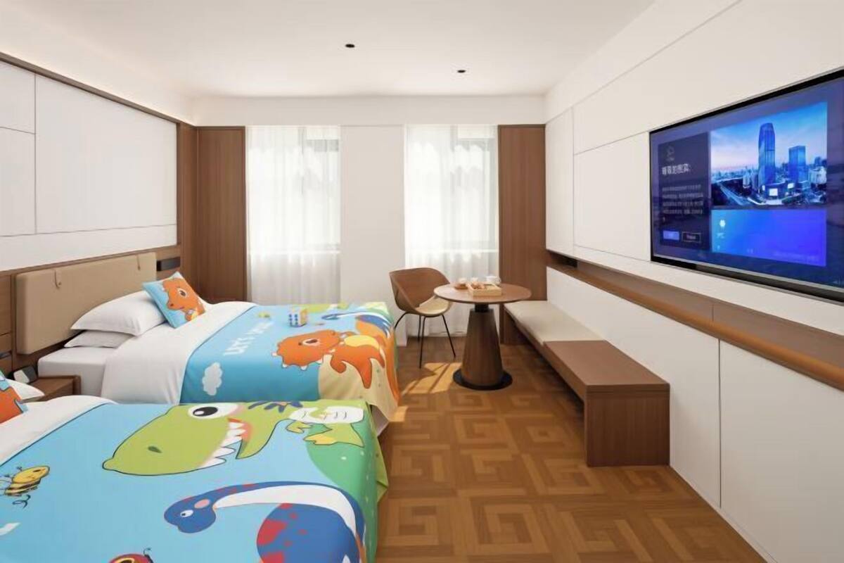 A hotel room with two beds, a TV, a small table, and a window with curtains.