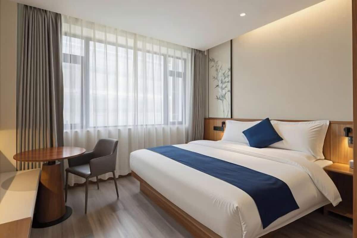 A hotel room with a large bed, a desk, a chair, and a window with curtains.