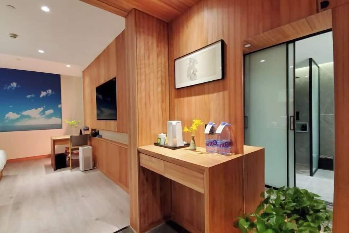 A modern hotel room with wooden paneling, a desk with amenities, a mounted TV, and a sliding door to a bathroom.