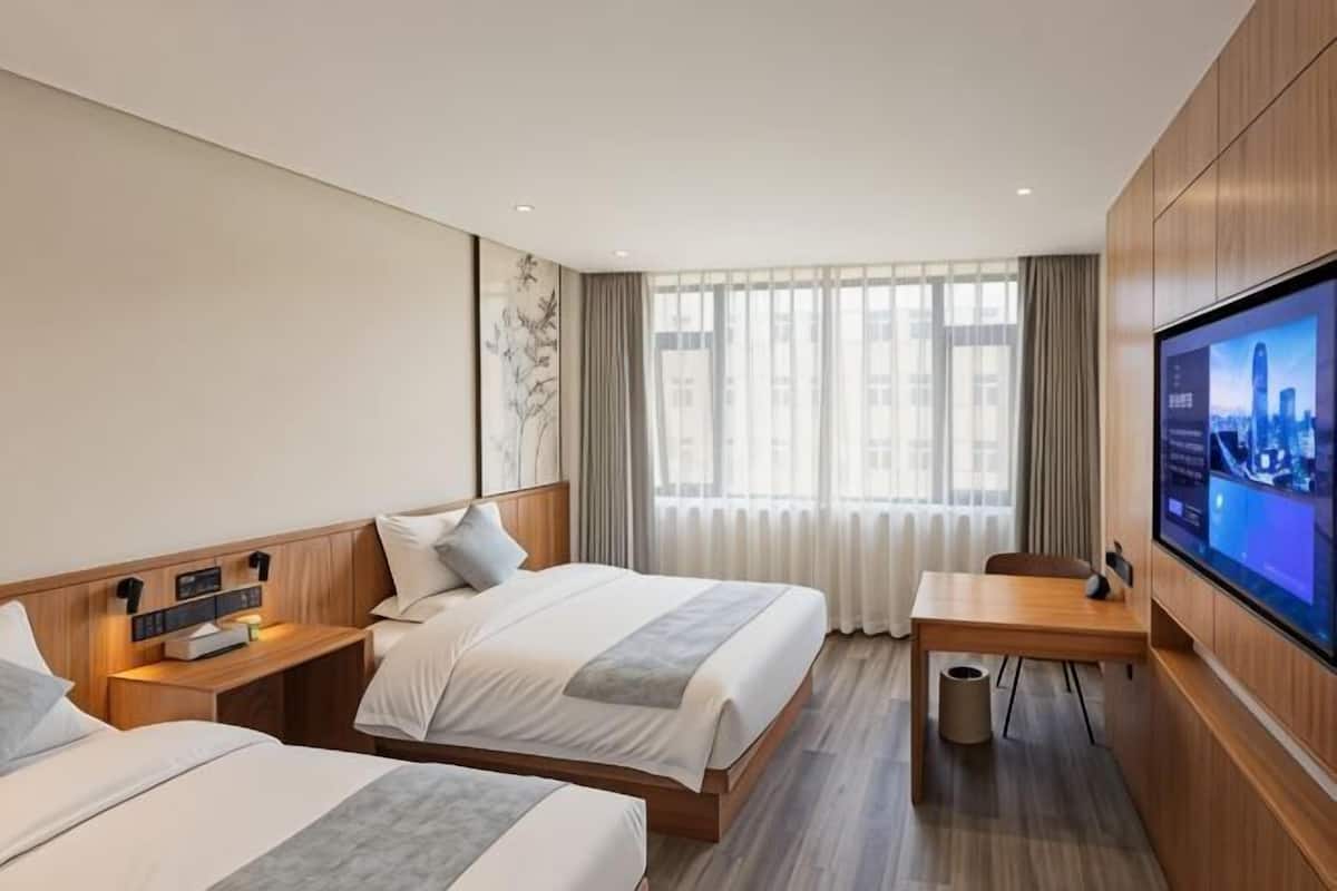 A hotel room with two beds, a TV, a desk, and a window with curtains.