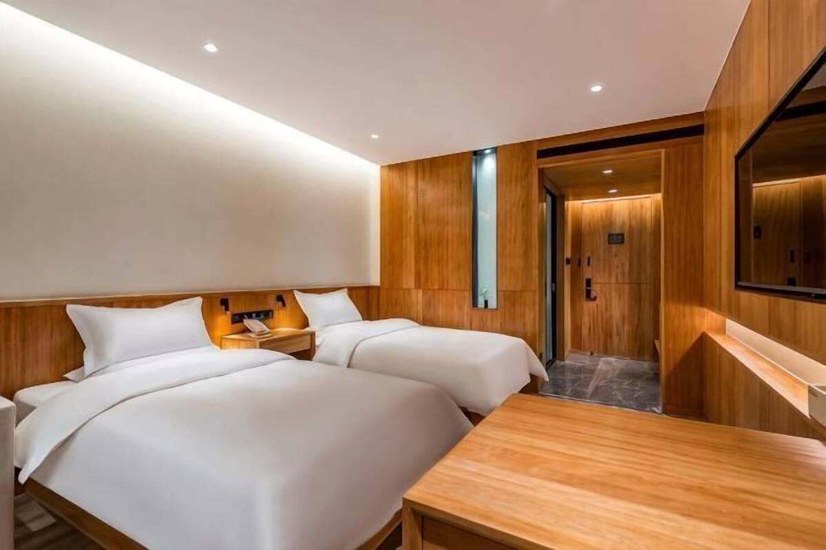 A hotel room with two beds, a wooden desk, a mirror, and a wooden wall panel.