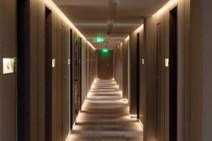 Un corridoio d'albergo con pavimento rivestito di moquette, porte su entrambi i lati e un cartello di uscita verde sul soffitto.