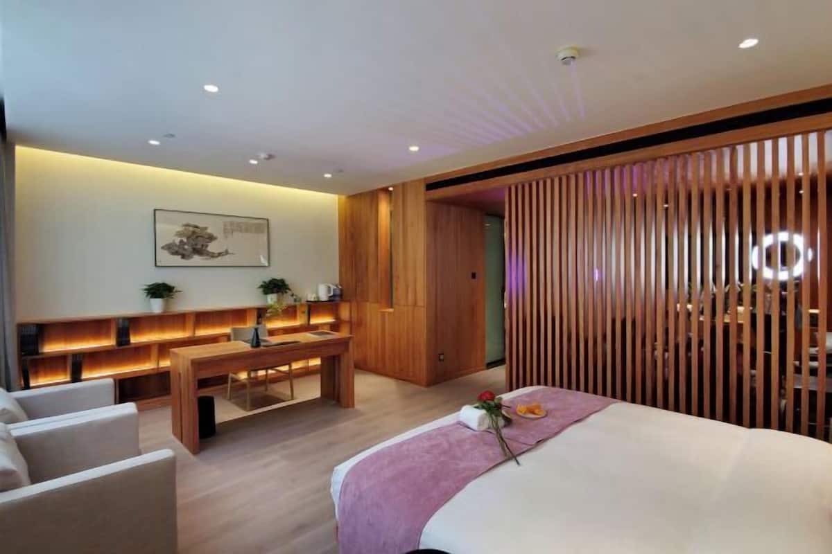 A modern hotel room with a bed, a desk, a sofa, and a wooden partition.