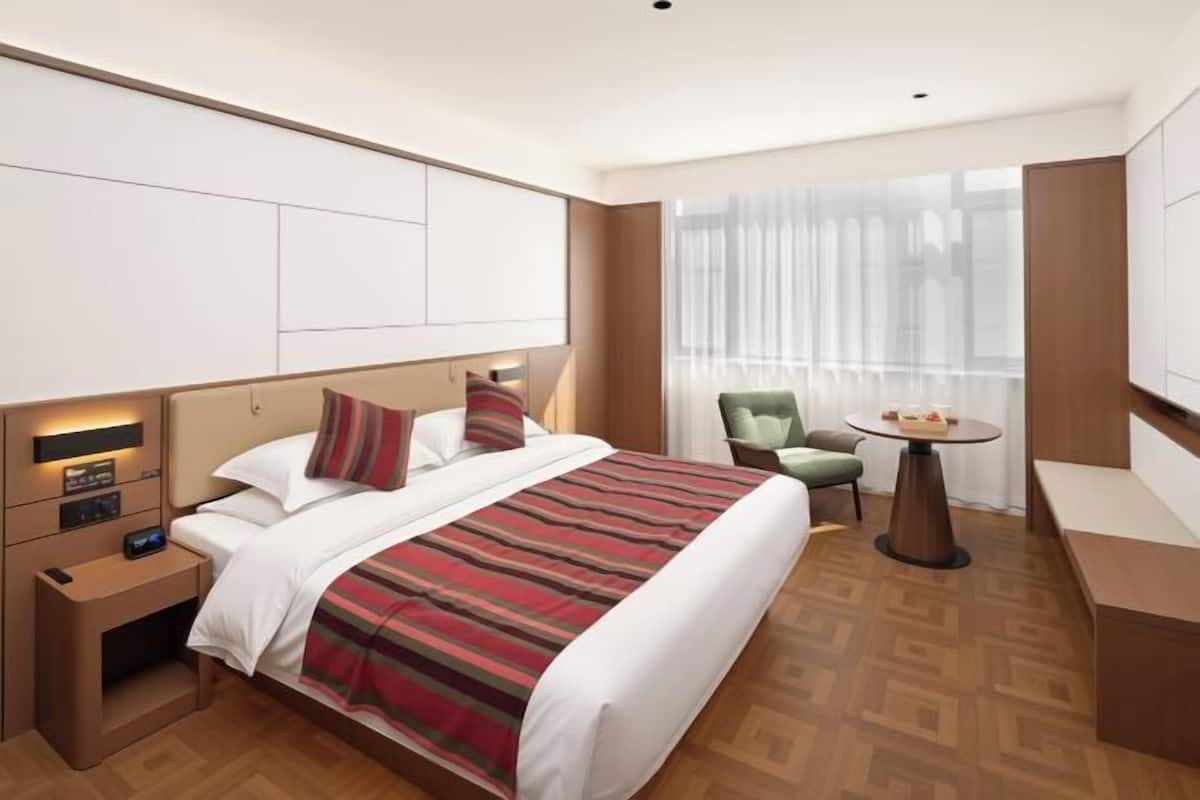 A hotel room with a bed, bedside table, lamp, chair, and a small table with a bowl of fruit.