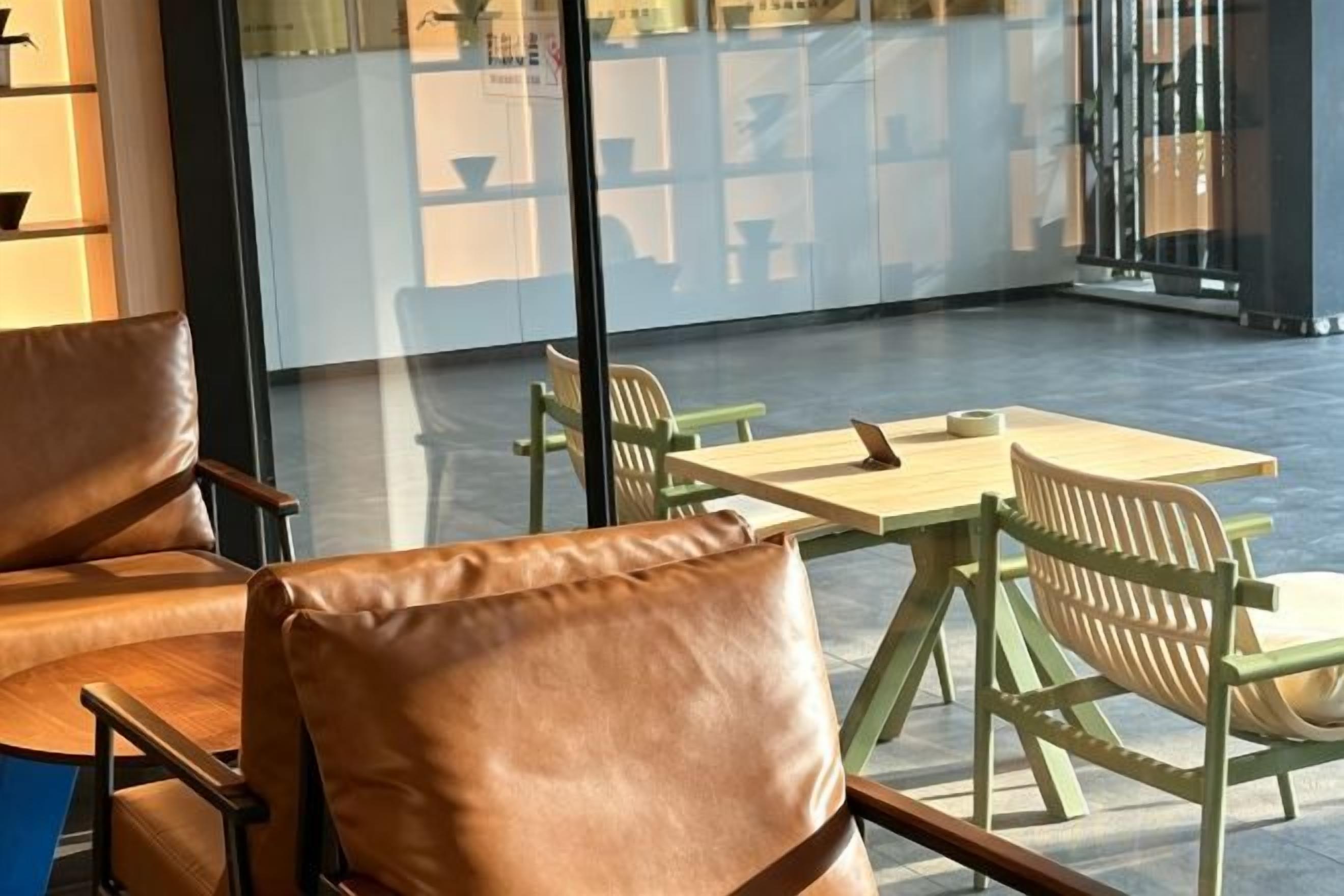 Un área de estar con sillones de cuero y una mesa de madera, una partición de vidrio y vistas a la calle.
