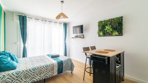 A bedroom with a bed, a desk, a chair, a TV, and a green wall decoration.