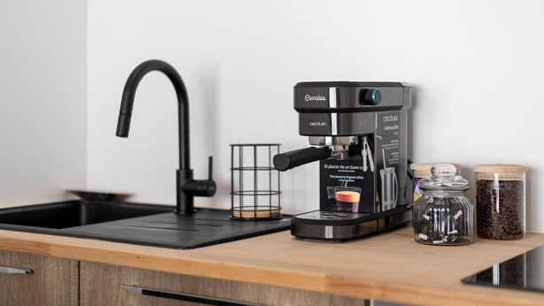 A modern kitchen with a black coffee maker, a glass coffee pot, and two jars of coffee beans on the counter.