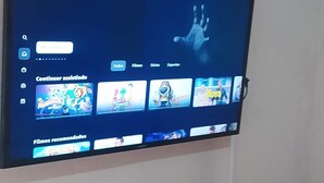 A television mounted on a wall displaying a streaming service interface with various content options. - Cozy mini house in Arraial d'Ajuda. (Arraial d'Ajuda)