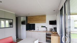 A modern kitchen with wooden cabinets, a sink, and a microwave. There is a dining area with a white table and chairs. - Chalet by Hegermeer With Lake Access (Heeg)