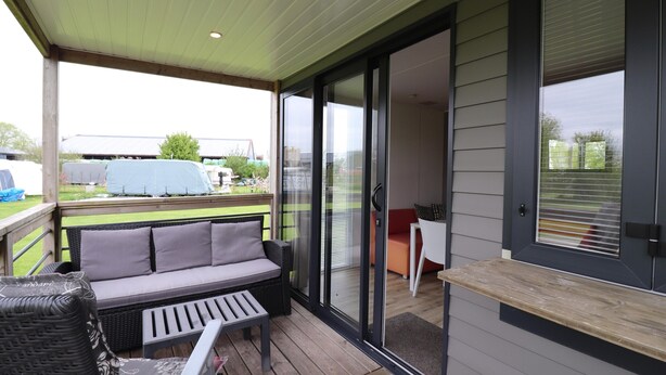 A covered patio with a sofa, a table, and a chair. - Chalet by Hegermeer With Lake Access (Heeg)