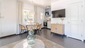 A modern kitchen with white cabinets, a built-in oven, and a microwave. There is a dining area with a round table and chairs, and a large window with curtains. - "Bliss"  stylish apartment with pool, by beach (Riviera Beach)