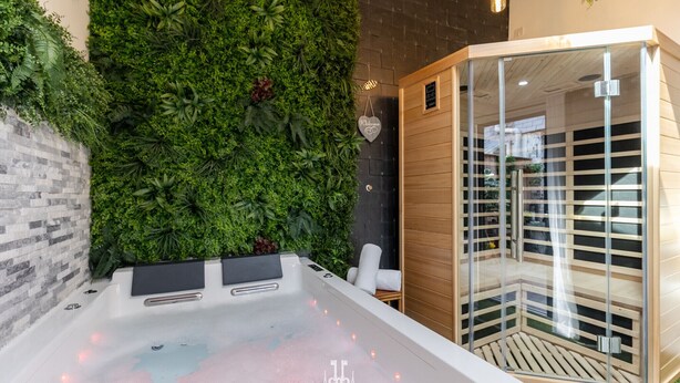 Un espace bien-être comprenant un jacuzzi, une douche en verre et un mur recouvert de verdure.