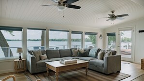 Ein geräumiges Wohnzimmer mit einer großen Eckcouch, einem Couchtisch und Blick auf einen See durch große Fenster.