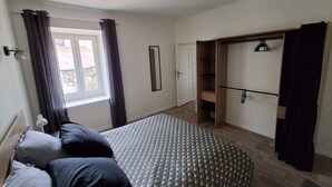 Un dormitorio con cama, armario, espejo y ventana con cortinas.