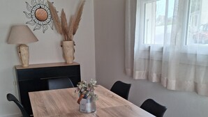 Un comedor con una mesa de madera, sillas negras, un florero con flores, una lámpara y un adorno en la pared.