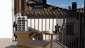 A terrace with a table and chairs, a coffee machine, and a view of a building with a tiled roof and chimney. - SCAPPO IN UMBRIA, L'attico del corso (Perugia)