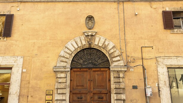 A building with a large wooden door, multiple windows with shutters, and a plaque on the wall. - SCAPPO IN UMBRIA, L'attico del corso (Perugia)