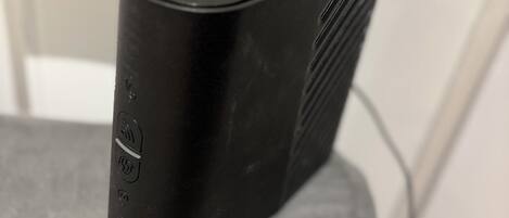 A black electronic device on a grey surface, possibly a speaker or charger, with a visible power cord.