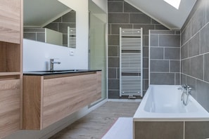 A modern bathroom with a wooden vanity, a large mirror, a bathtub, and a towel rack. - Holiday Home in La Roche Near Center (La Roche-en-Ardenne)