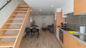 A modern kitchen with wooden cabinets, a dining area with a table and chairs, and a staircase leading to an upper level. - Holiday Home in La Roche Near Center (La Roche-en-Ardenne)