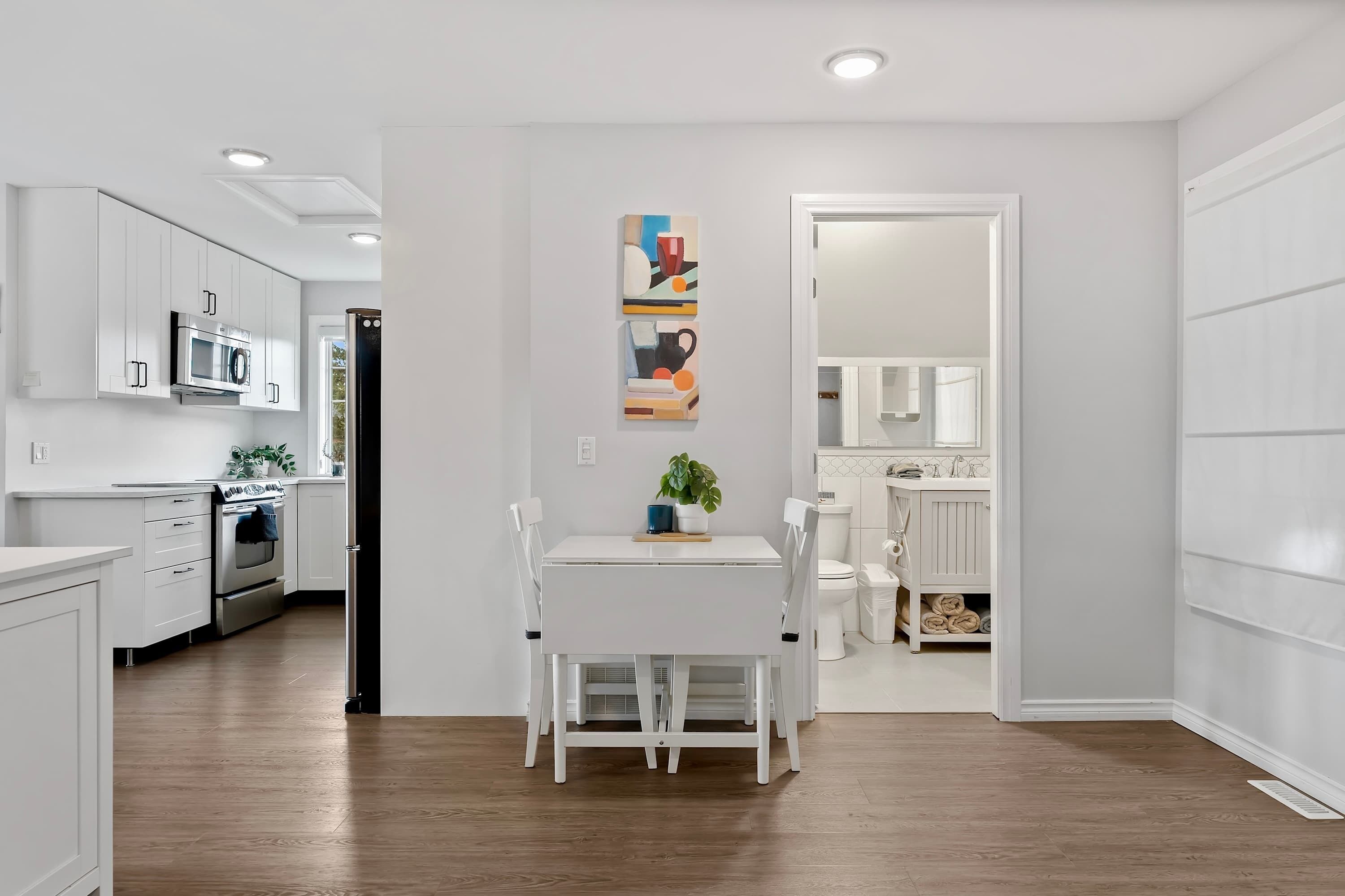 Une cuisine moderne avec des meubles blancs, un four à micro-ondes encastré et un coin repas comprenant une table et des chaises blanches.