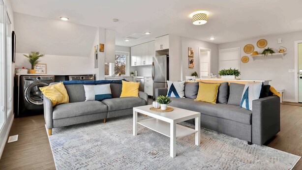 Un salon moderne avec un canapé gris, une table basse blanche et une cuisine en arrière-plan.