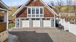Une maison à deux étages avec un garage, une terrasse couverte et une allée gravillonnée.