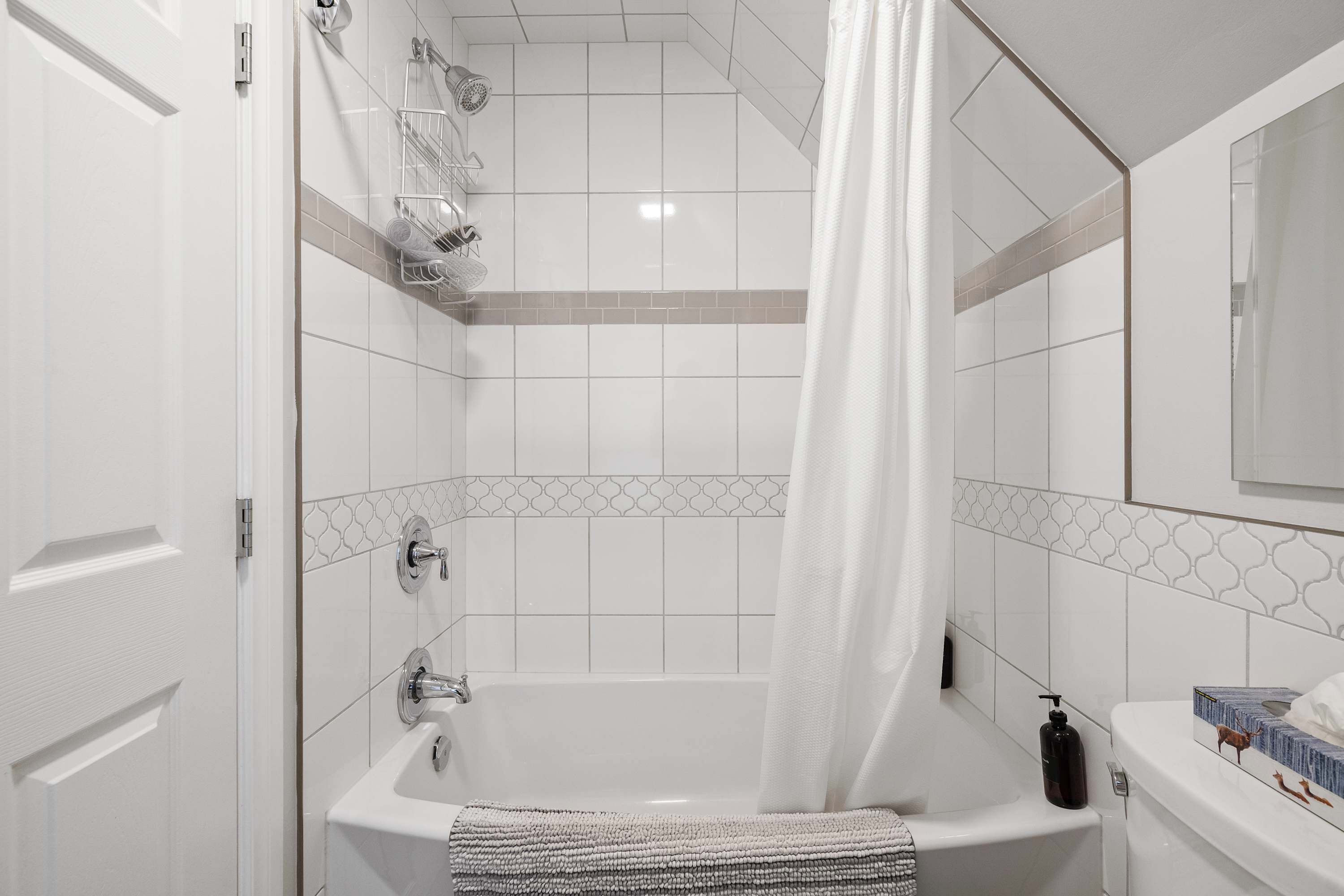 A modern bathroom with a bathtub, a shower, and a toilet. There is a towel rack above the bathtub and a bottle of shampoo on the toilet.