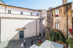 A narrow cobblestone street with buildings on either side, a few people walking, and a small outdoor seating area with umbrellas. - S.Angelo Apartments (Rome)