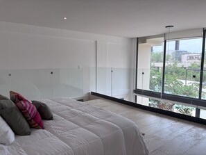 A modern bedroom with a large bed, a glass partition, and a view of the city. - Modern apartment in Tulum trendy zone, pool and wifi (tulum)