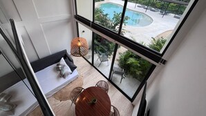 A balcony with a view of a swimming pool, a round table with chairs, and a hanging light fixture. - Modern apartment in Tulum trendy zone, pool and wifi (tulum)
