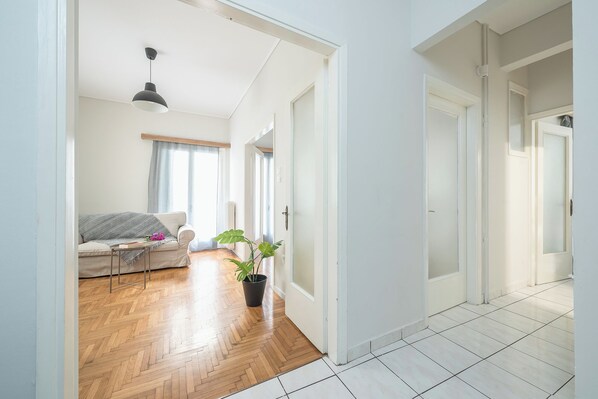 A bright, open living area with a wooden floor, a sofa, a coffee table, and a potted plant. - 2BD - Center of Athens - 4mins Walk To Acropolis (Athina)