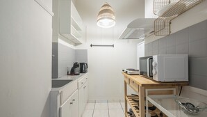 A narrow kitchen with white cabinets, a wooden table, a hanging light fixture, and a microwave. - 2BD - Center of Athens - 4mins Walk To Acropolis (Athina)