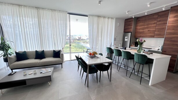 Eine moderne Küche mit einer zentralen Kochinsel, einem Essbereich mit Tisch und Stühlen sowie eine Sitzecke mit Blick ins Freie.