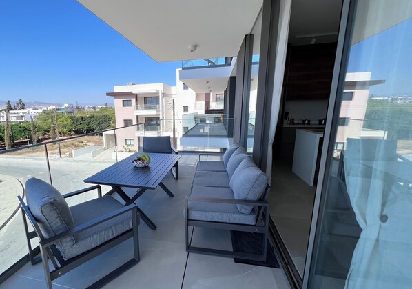 Un balcón con una mesa y sillas de comedor, un sofá y una zona de cocina.