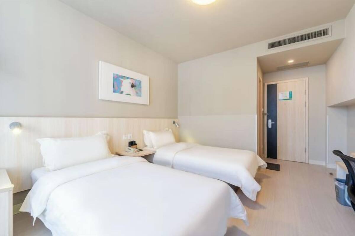 A hotel room with two beds, a small desk, a chair, a picture on the wall, and a door leading to another room.
