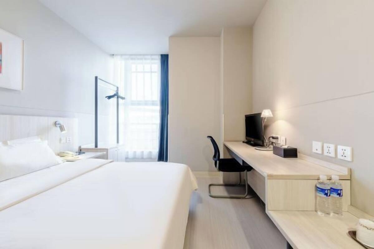 A hotel room with a bed, desk, chair, TV, lamp, and a window with curtains.