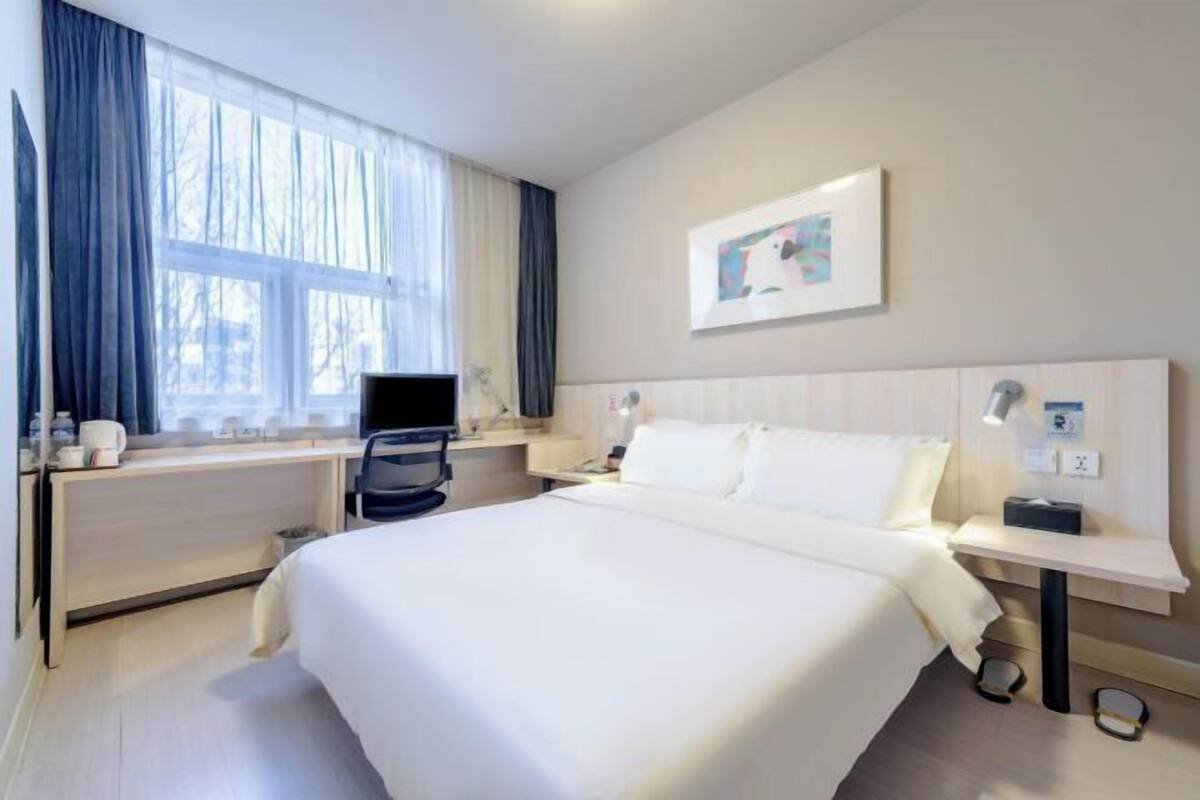 A hotel room with a large bed, a desk, a chair, a TV, and a window with curtains.