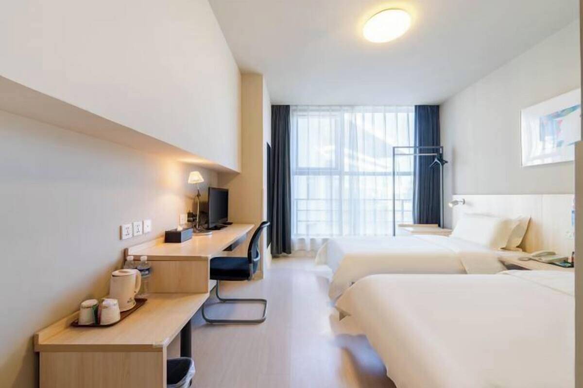 A hotel room with a desk, two beds, a TV, and a window with curtains.