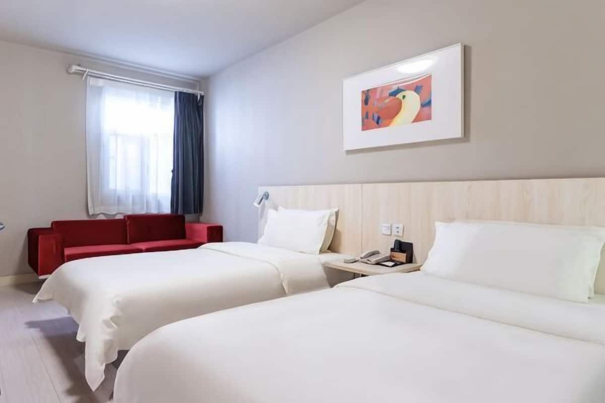 A hotel room with two beds, a red sofa, a painting on the wall, and a window with curtains.