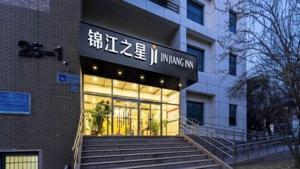 Entrada de um hotel com uma placa indicando 'JINJIANG INN' e uma escadaria que leva à entrada.