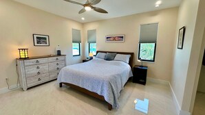 A bedroom with a bed, dresser, bedside tables, ceiling fan, and windows. - Beachcomber Lodge in Fort Myers Beach (Fort Myers Beach)