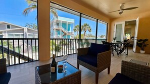 A balcony with wicker furniture, a table with a bottle and glasses, and a view of a blue building and palm trees. - Beachcomber Lodge in Fort Myers Beach (Fort Myers Beach)
