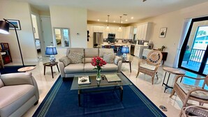A modern living room with a sofa, coffee table, and chairs, a kitchen in the background, and a balcony with a view. - Beachcomber Lodge in Fort Myers Beach (Fort Myers Beach)
