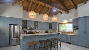 Una cucina moderna con isola centrale, sgabelli da bar, elettrodomestici in acciaio inossidabile e luci a sospensione.