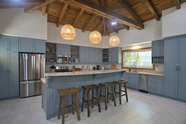 A modern kitchen with a central island, bar stools, stainless steel appliances, and pendant lighting.