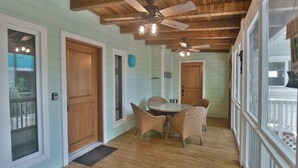 Un portico coperto con una ventola a soffitto, un tavolo da pranzo con sedie e porte in legno.