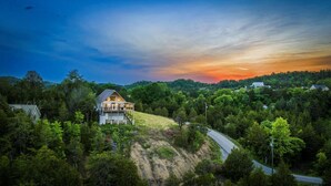 A house with a large porch and a view of the surrounding forest. - Tennessee Whiskey Cabin- Lake and Mtn Views, Covered Deck, Game Room, Pool Table, BBQ, Pets (Sevierville)